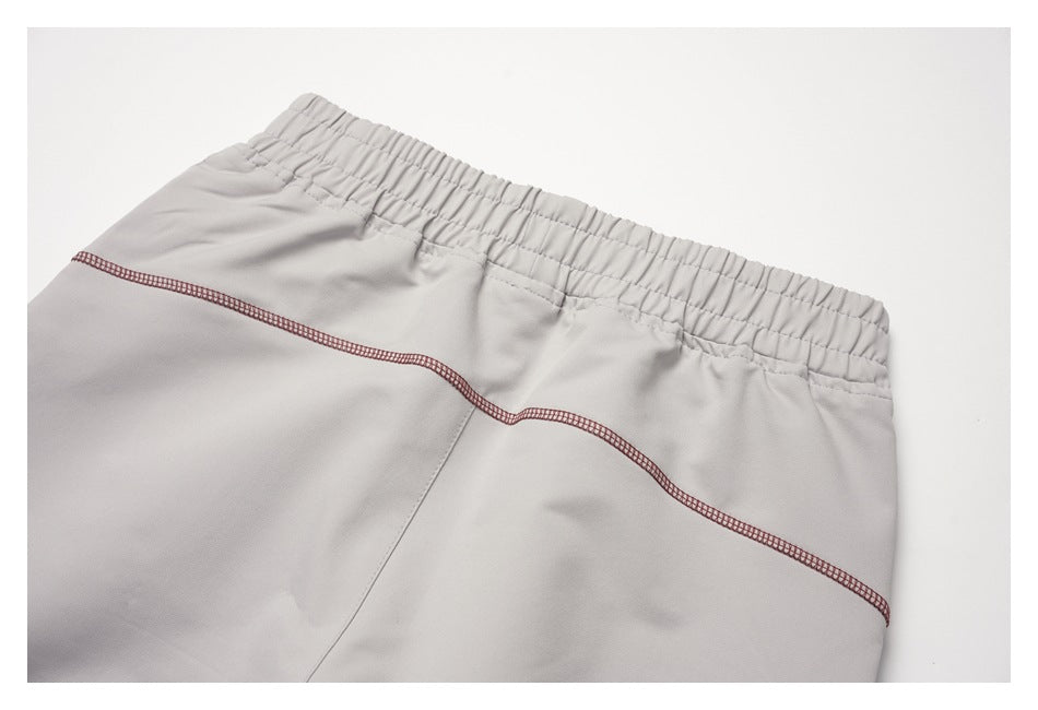 Close-up of light gray shorts with an elastic waistband and a curved burgundy overlock seam.
