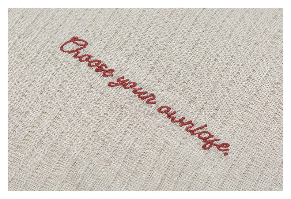 Close-up of red cursive embroidery on beige, subtly striped knit fabric.