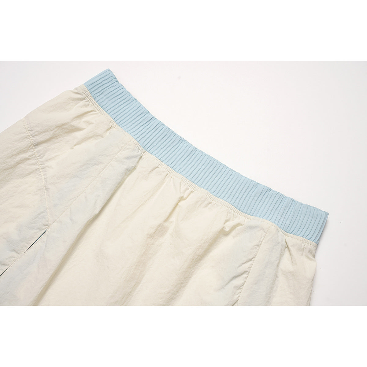 Close-up of an ivory skirt with a pale blue ribbed elastic waistband and stitched panel seams.