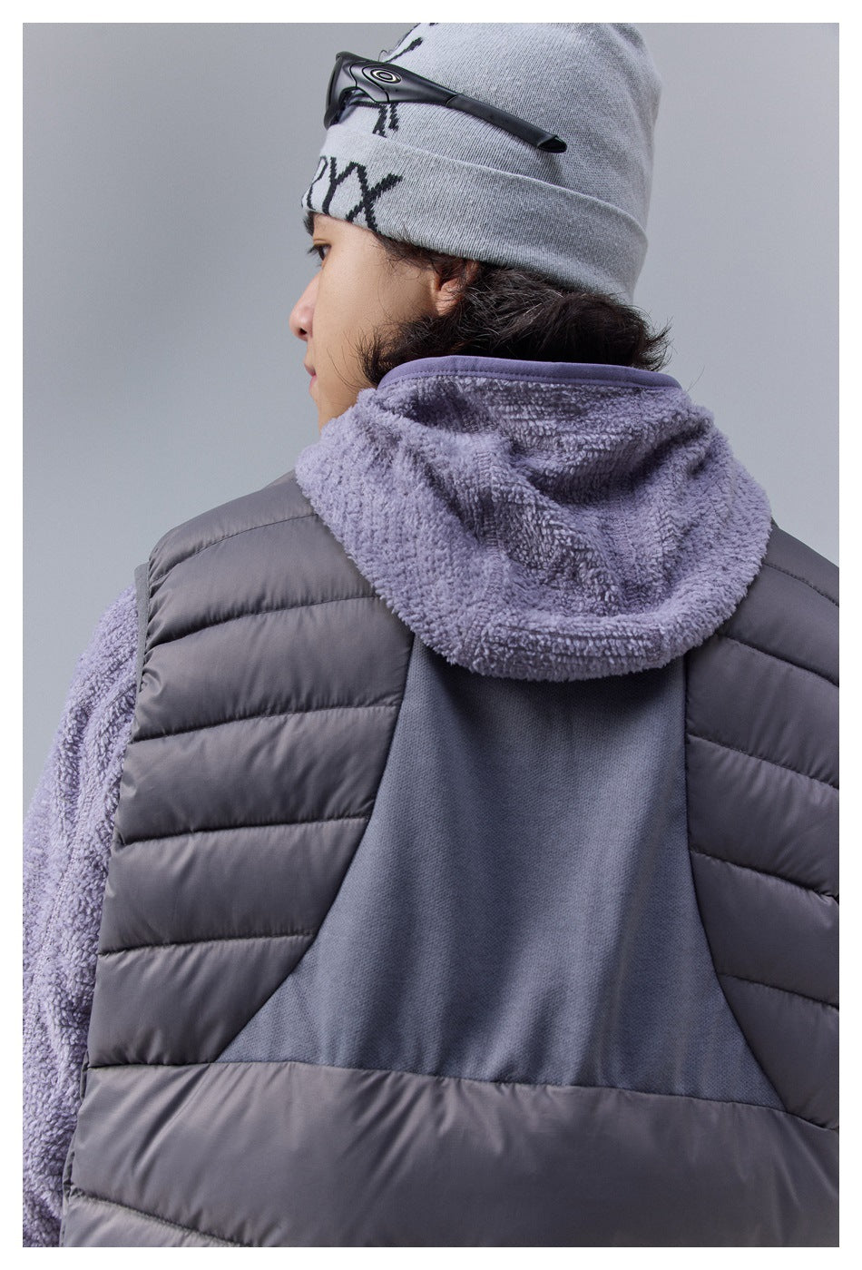 Close-up rear view of a charcoal quilted vest with a gray knit back panel and textured hood.