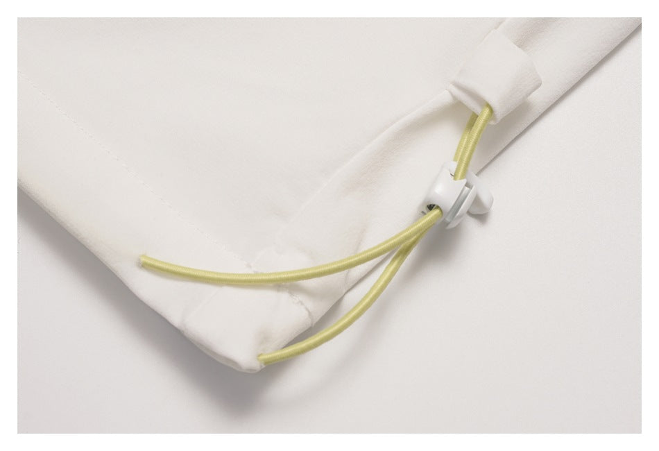 Tight close-up of pale yellow cords and a white toggle attached to the hem of a white garment.