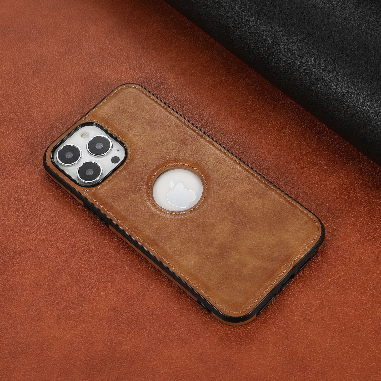 A smartphone with an iPhone 16 Pro Max Case - Premium Synthetic Leather, Shockproof, Anti-Fingerprint Protective Cover in brown, showcasing a triple camera setup and an Apple logo, lying on a leather surface.
