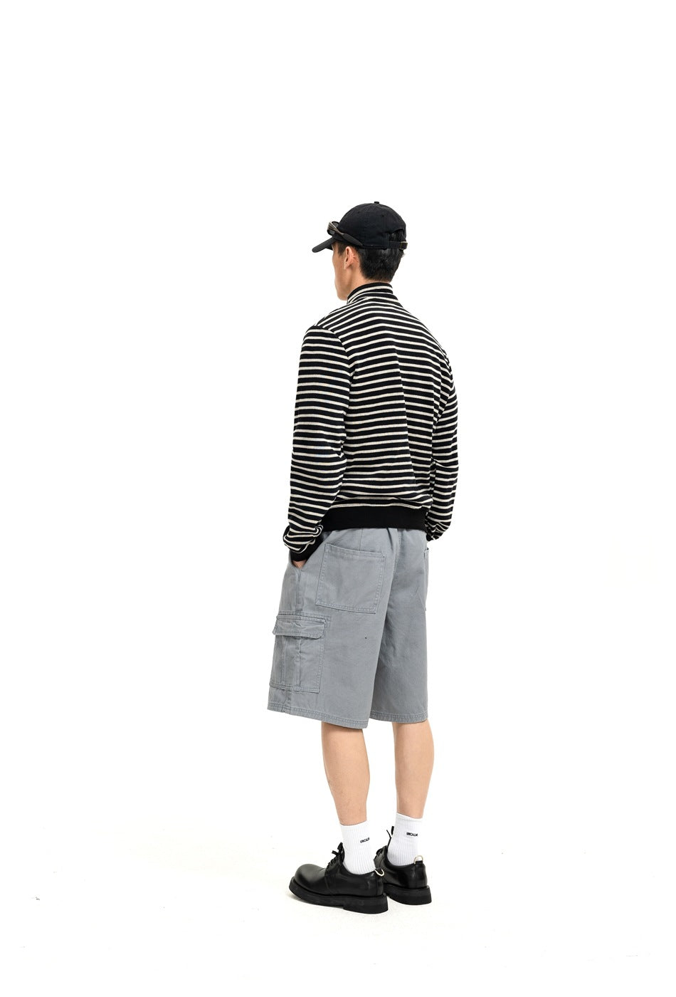 Rear three-quarter view of a person wearing a black-and-cream striped jacket and light gray cargo shorts.