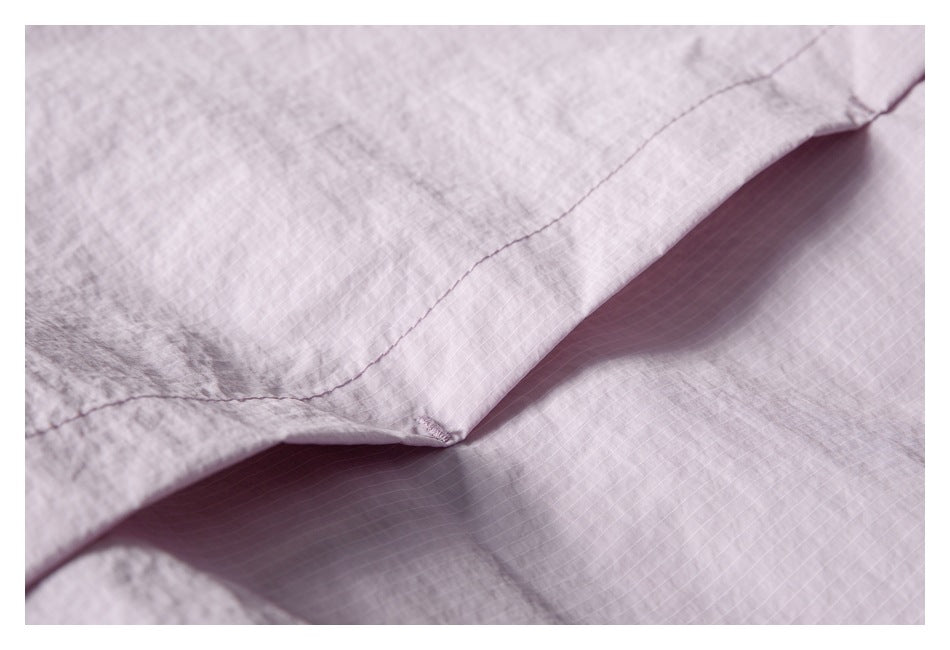 Close-up of a stitched seam and overlapping panels on pale pink grid-patterned fabric.