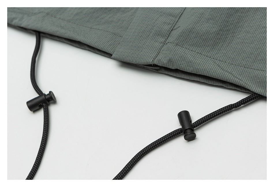 Close-up of black cord adjusters beneath a hem on muted gray-green ribbed fabric.