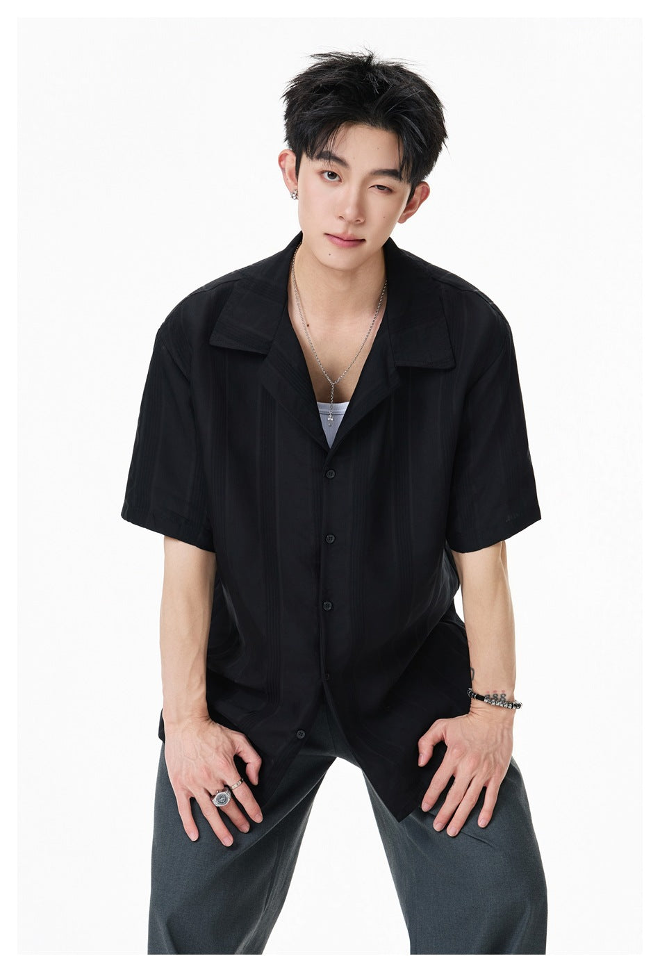Model in a black striped short-sleeve button-up shirt with a wide collar, shown from the front.