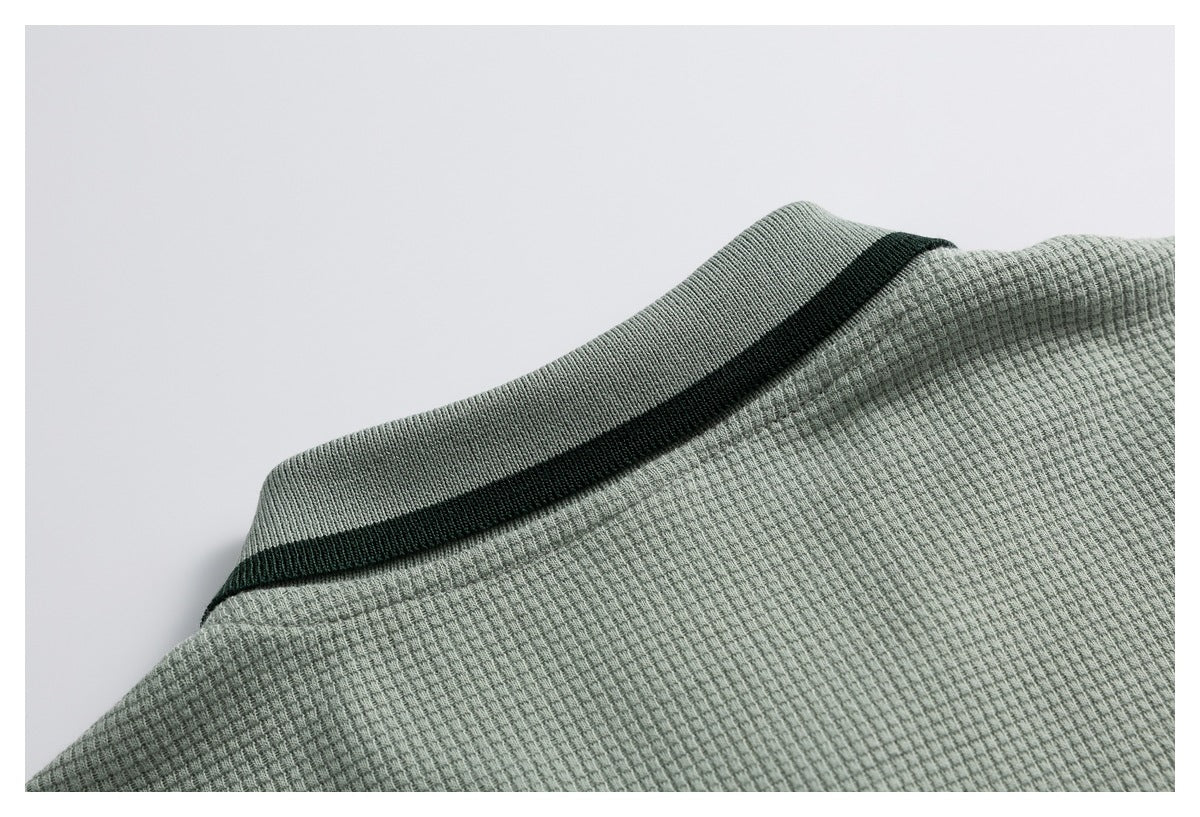 Close-up of a sage green textured garment neckline with dark green striped trim.