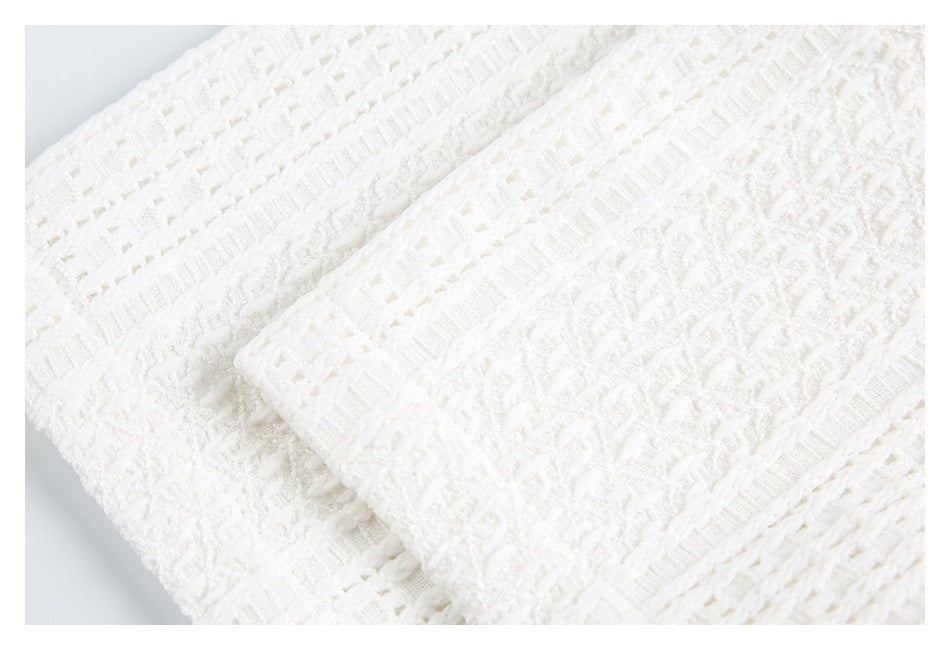 Close-up of layered white textured knit with raised motifs and openwork stripe detailing.