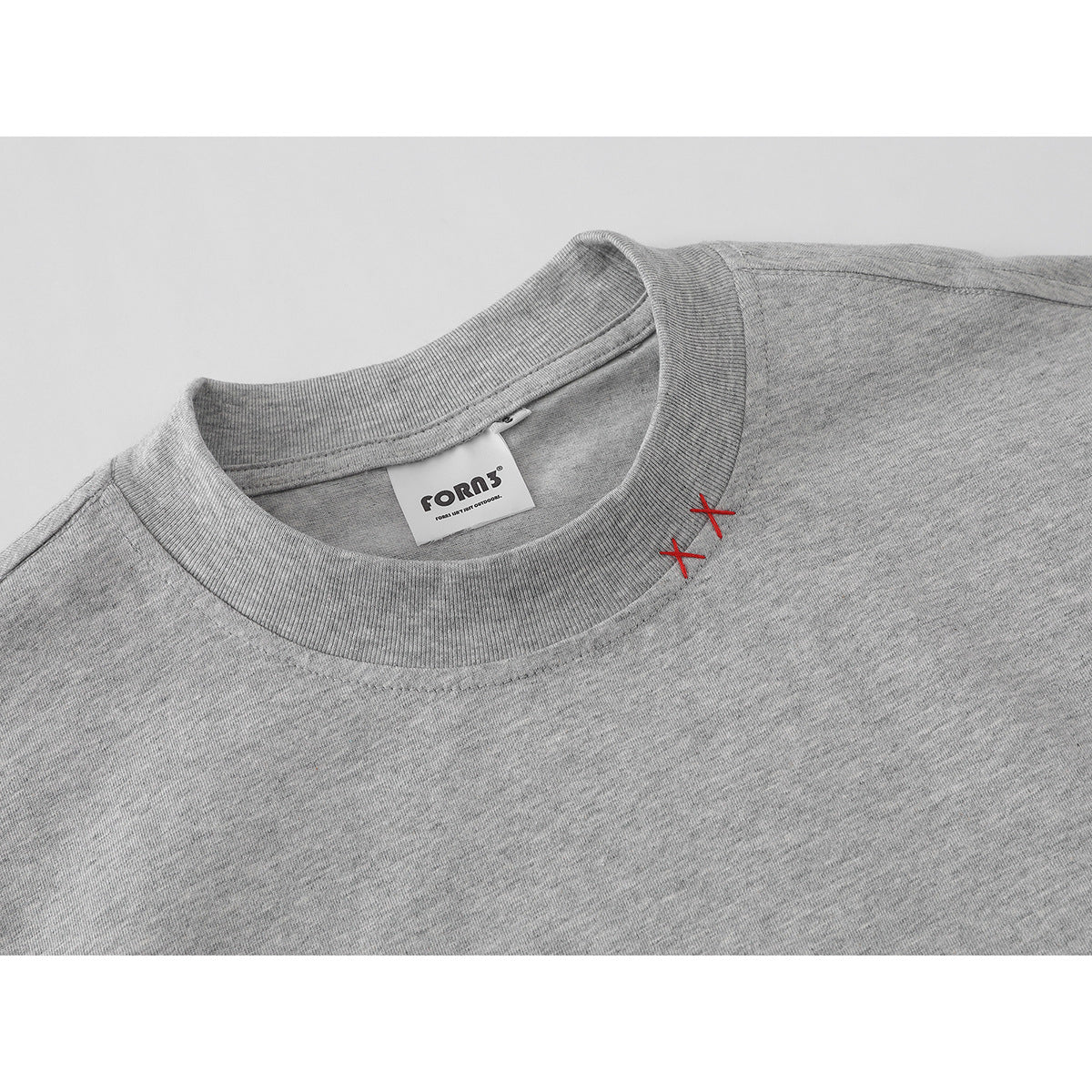 Close-up of a heather-gray T-shirt crew neck with a white brand label and two red cross stitches.