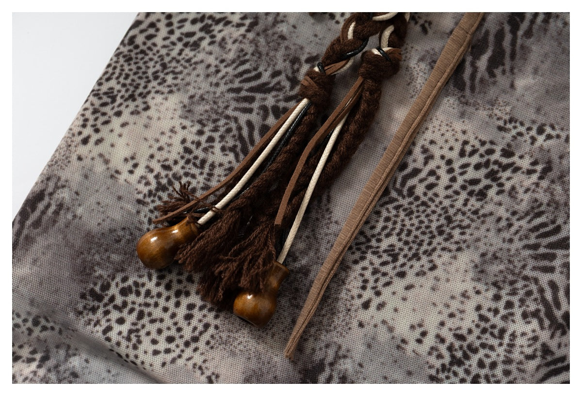 Close-up of dark braided tassels with wooden ends resting on gray-brown animal-print fabric.