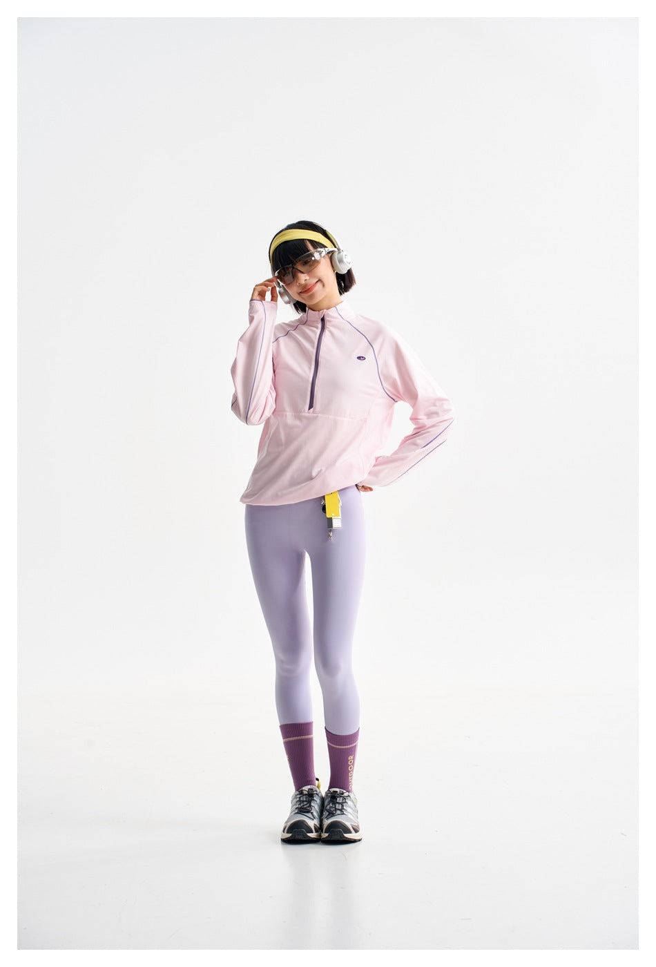 Model posing in a pale pink half-zip top with lavender piping and light lavender leggings.