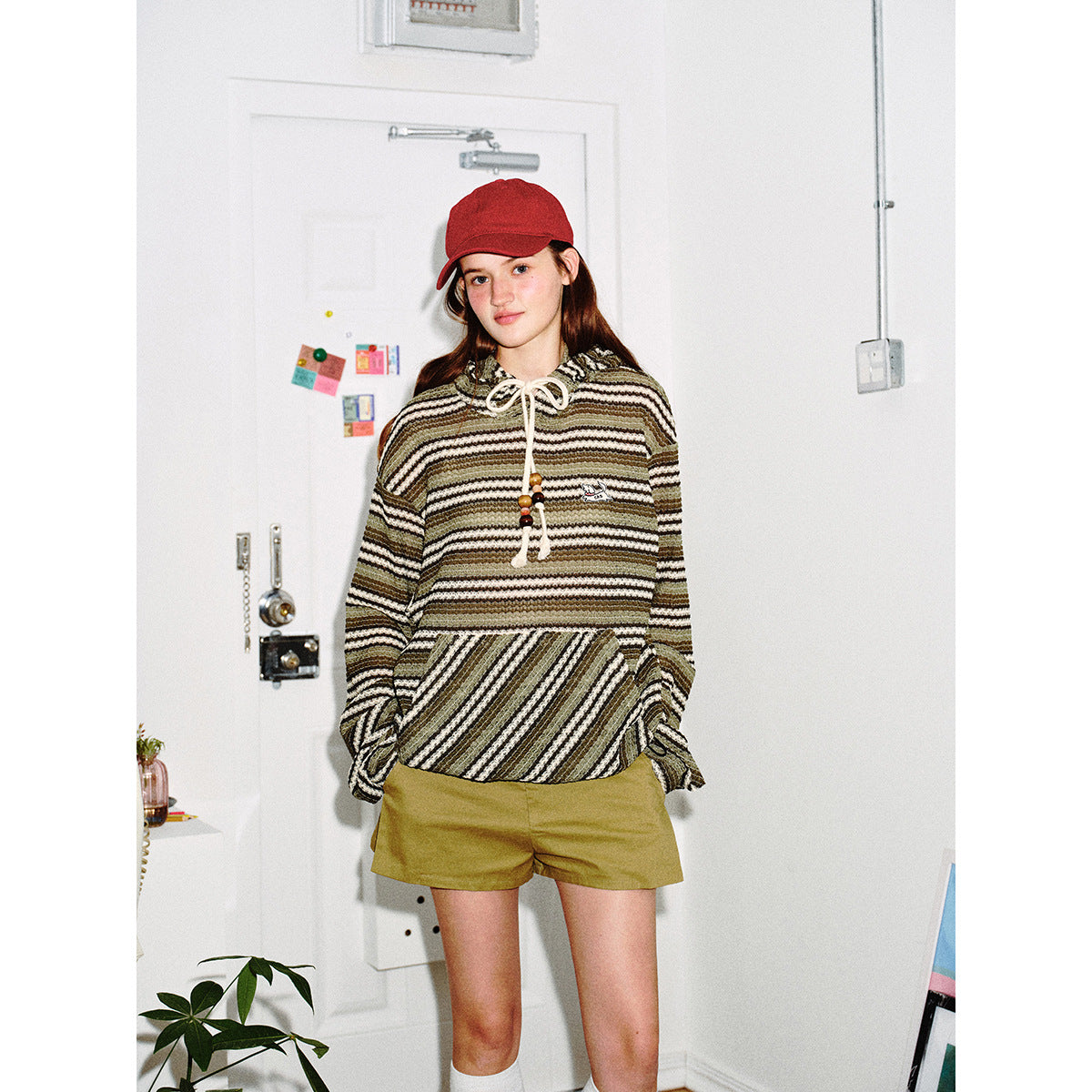 Front view of a model in an olive, cream and black striped hoodie with a large pocket and olive shorts.