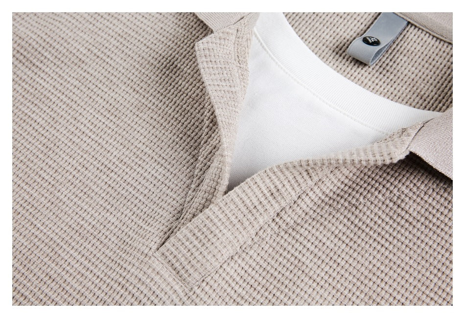 Close-up of a beige textured collared top showing the neckline, white inner layer, and a small tab with a dark oval mark.