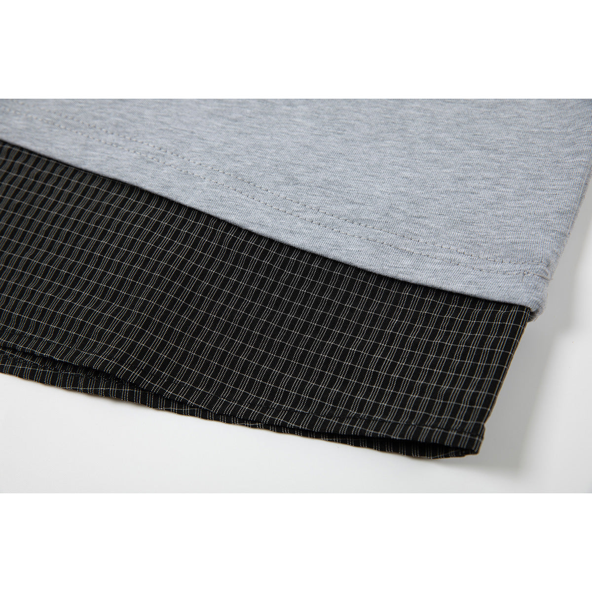 Close-up of the gray shirt hem overlapping a black fine-check fabric panel.