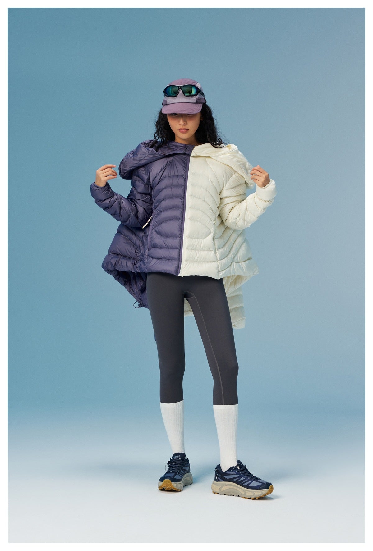 Model wearing a two-tone cream and purple hooded puffer jacket with black leggings and white socks.