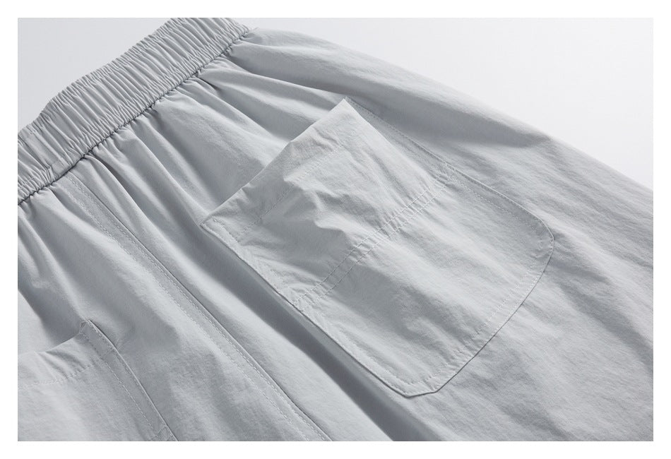 Close-up of a stitched patch pocket on light gray shorts, with part of the elastic waistband visible.
