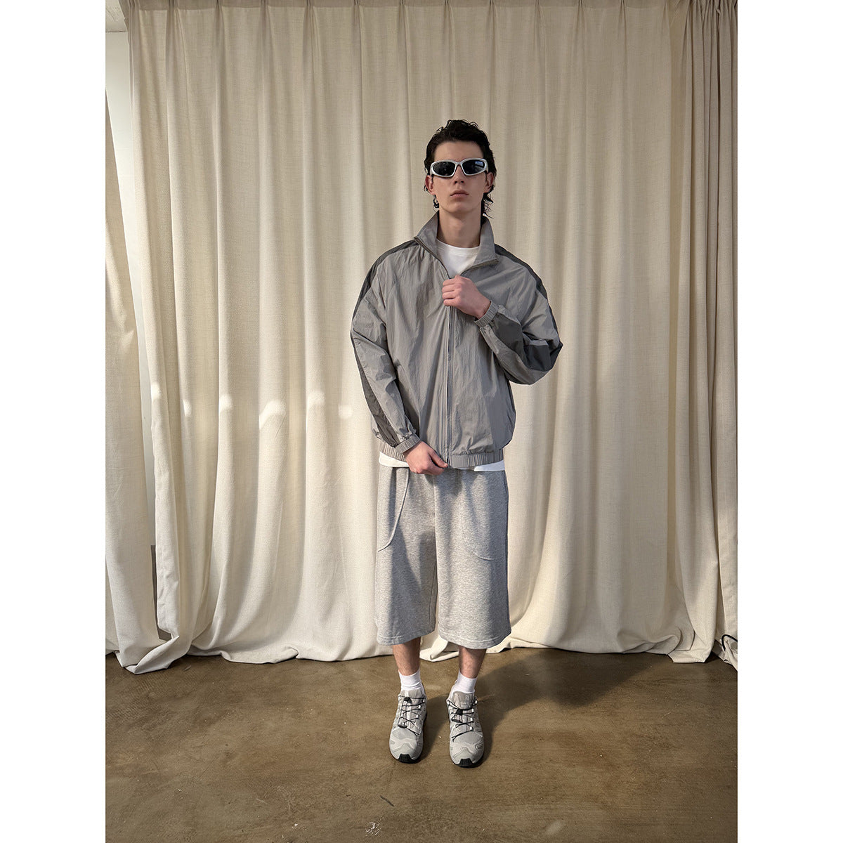 Full-length front view of a model wearing a light gray zip jacket with dark sleeve panels and gray shorts.