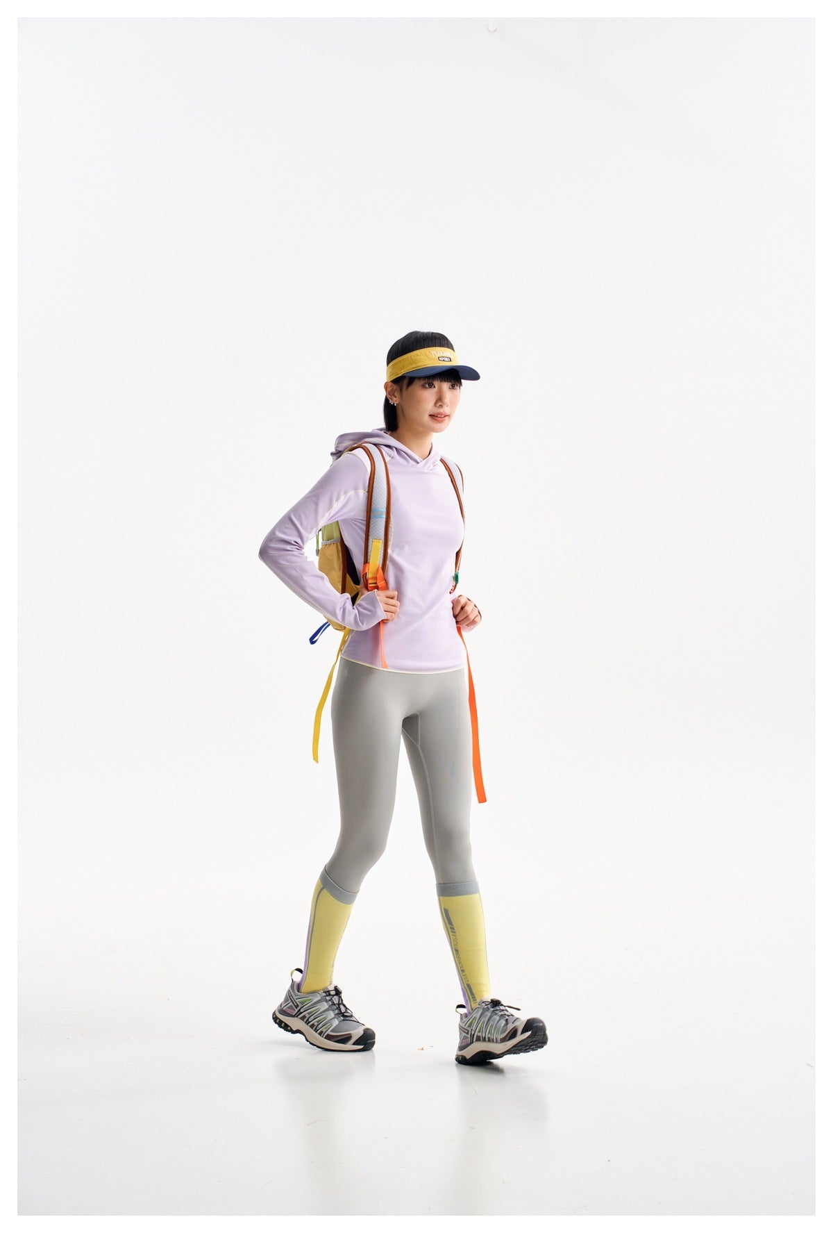 Model in a lavender hoodie and gray leggings, shown at an angle wearing a colorful backpack and yellow socks.