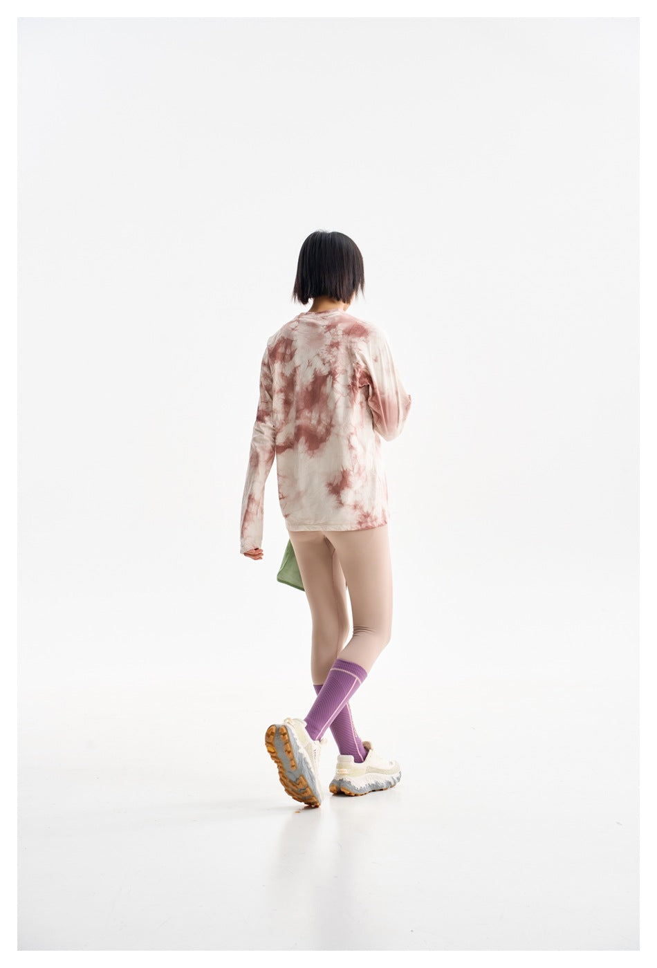 Rear view of a model wearing a cream and dusty pink tie-dye long-sleeve top, beige leggings and purple socks.