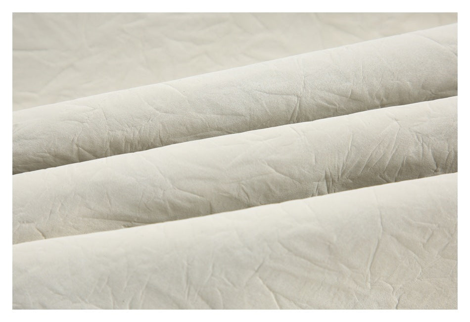 Close-up of ivory fabric folded into overlapping bands, showing its softly creased surface.