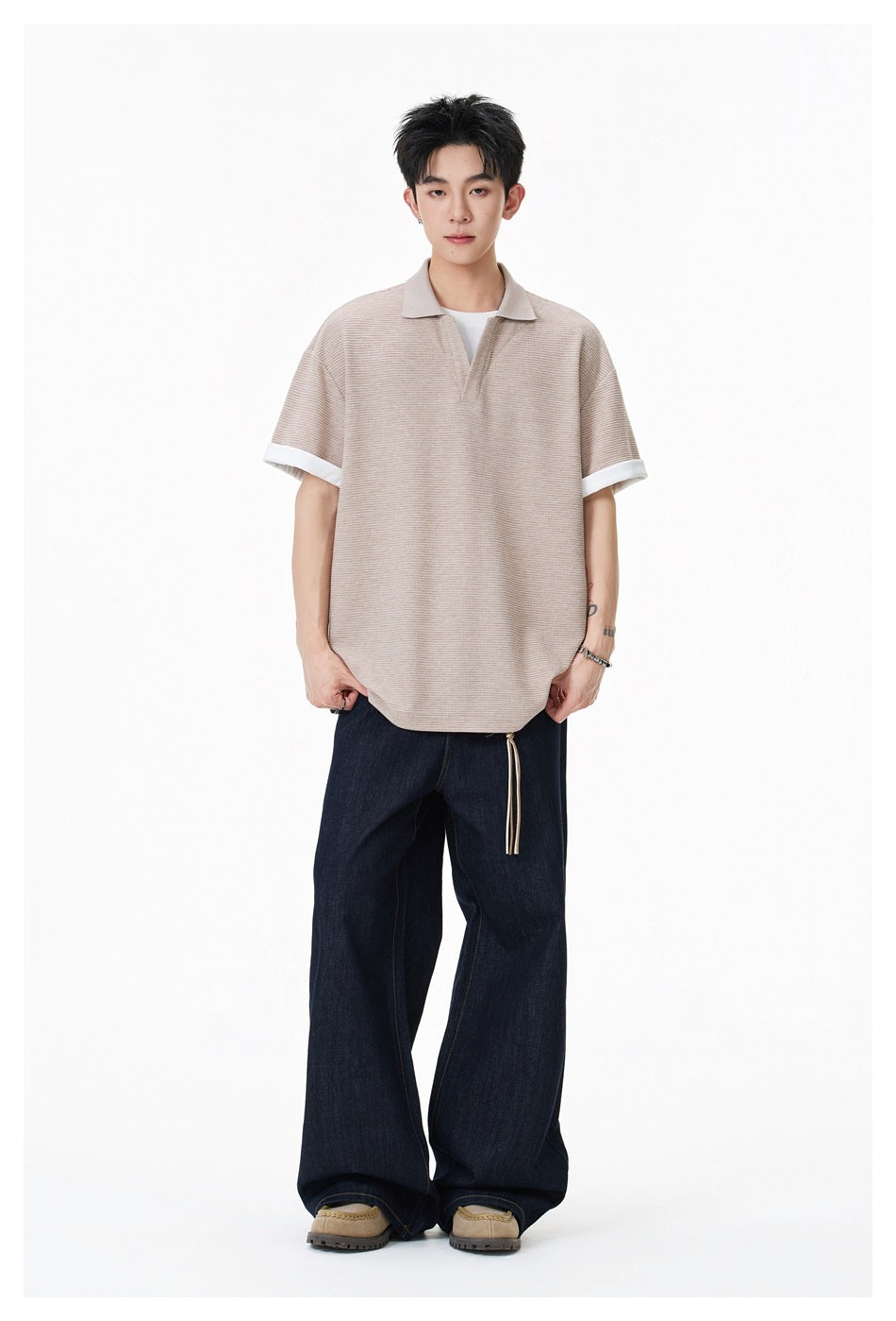 Full-length front view of a model wearing a beige textured polo with white turned-up cuffs and dark wide-leg jeans.