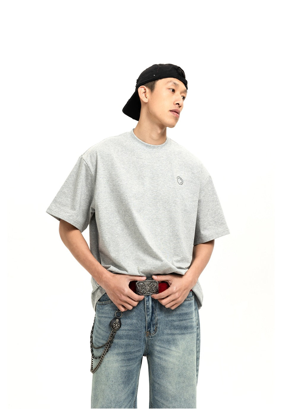 Model wearing a gray T-shirt with a small dark chest emblem and blue jeans; front view.
