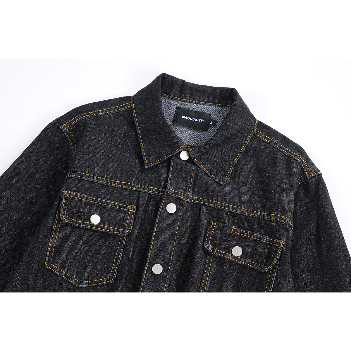 Close-up of a black denim jacket front with pointed collar, silver snaps, two flap pockets, and gold stitching.