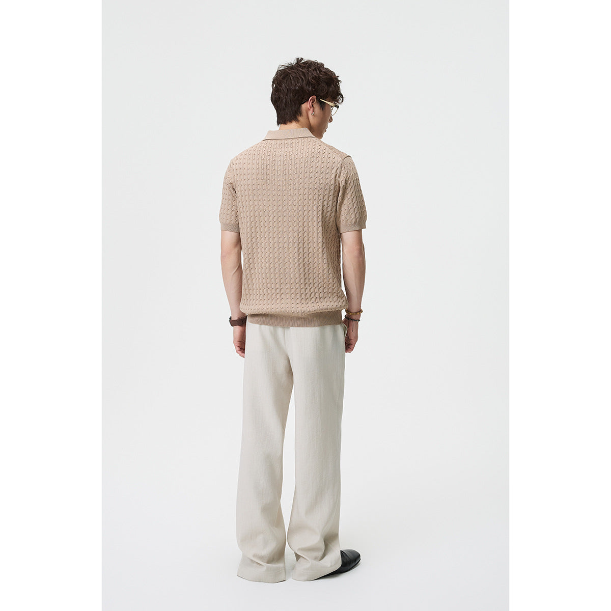 Back view of a model wearing a taupe textured polo and loose ivory trousers.