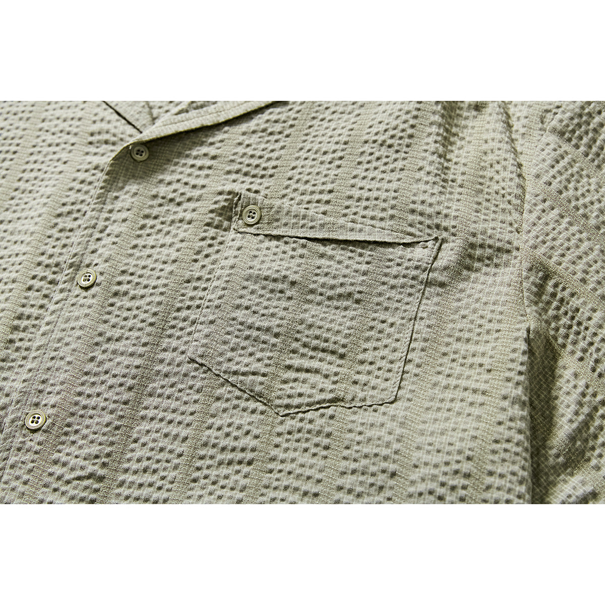 Close-up of a sage-gray textured shirt showing its button placket and single chest pocket.