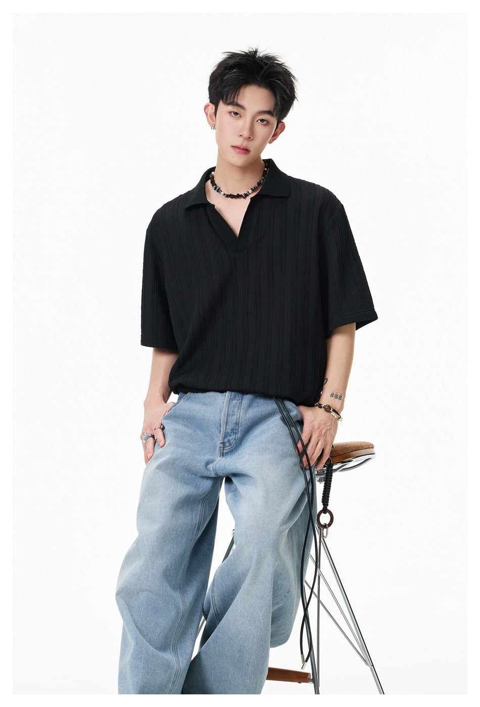 Model wearing a black textured short-sleeve polo with light blue jeans, shown from the front.