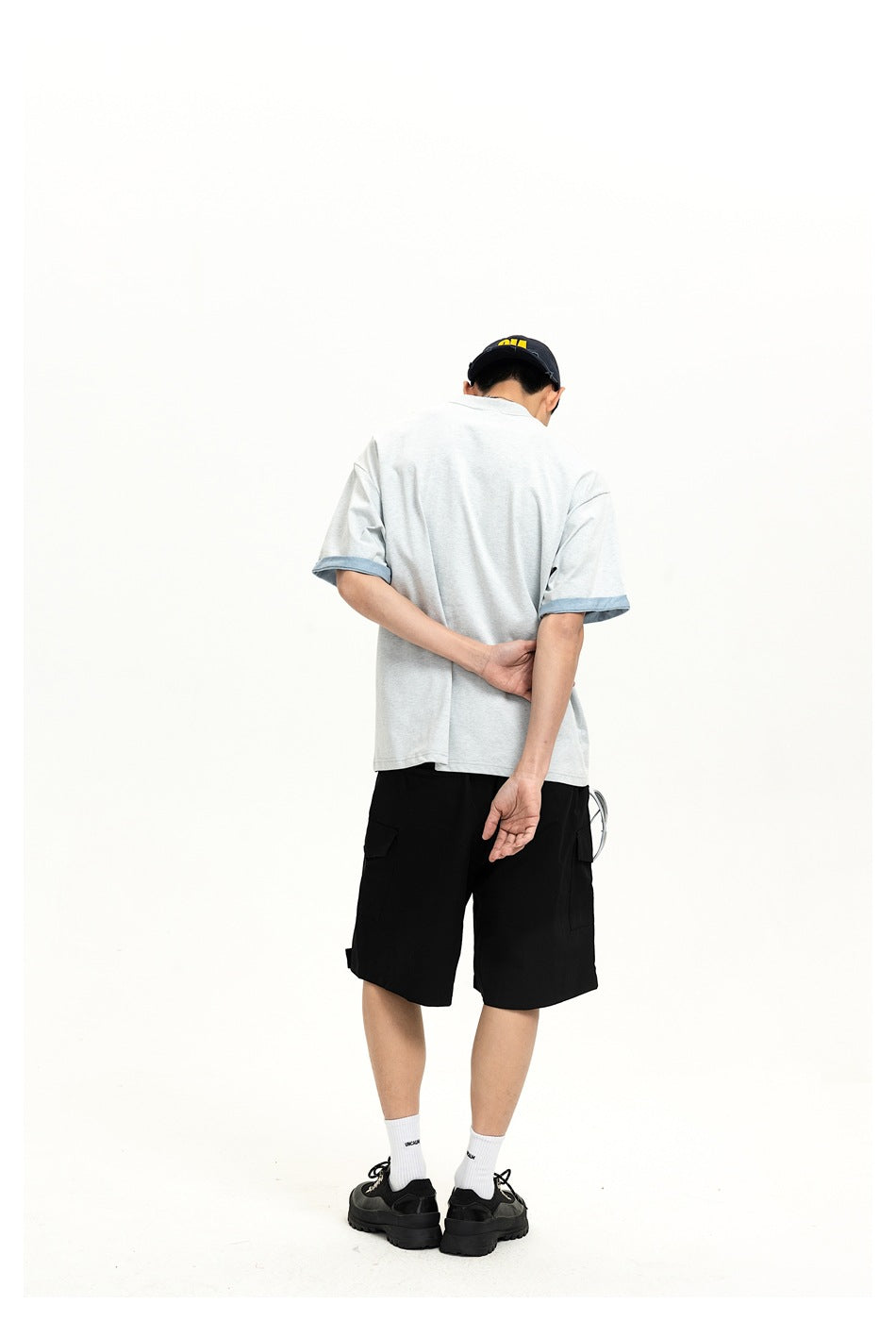 Back view of a model wearing a light gray T-shirt with blue sleeve cuffs and black shorts.