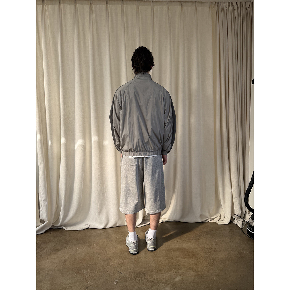 Rear view of a model wearing a light gray jacket with dark shoulder panels and an elastic hem.