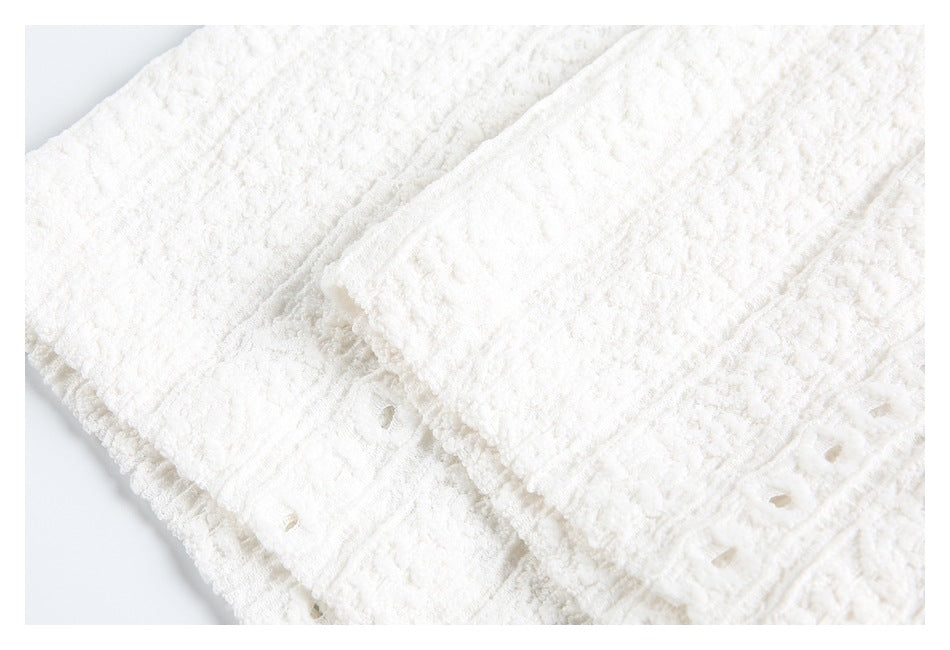 Close-up of a folded sleeve cuff on a white textured garment with eyelet detailing.