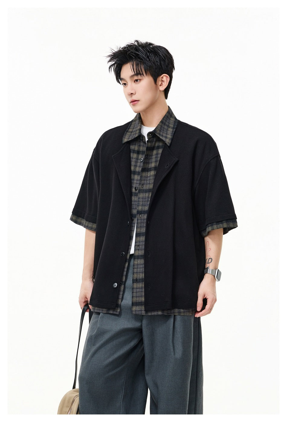 Model wearing a black button-front short-sleeve overshirt with dark plaid collar, cuffs and hem over a plaid shirt.