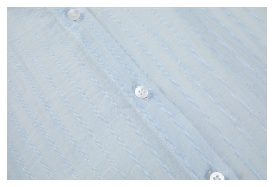 Close-up of pale blue striped shirt fabric and white buttons along the front placket.