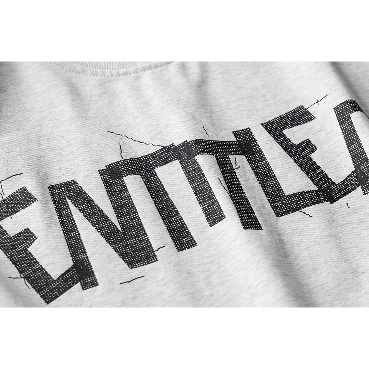 Close-up of the black distressed lettering printed across a light gray heather T-shirt.