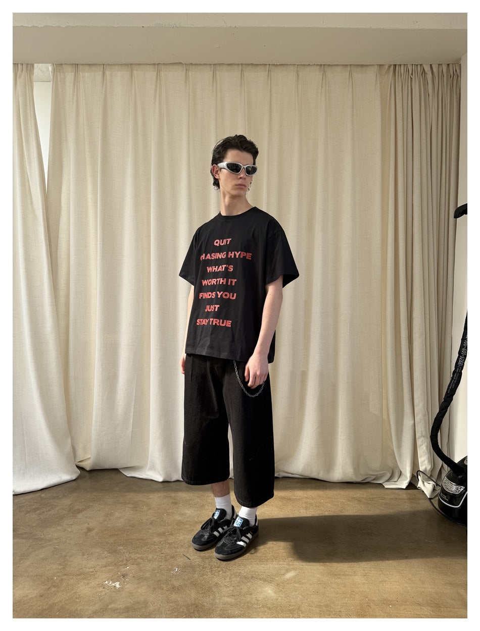 Model in a black T-shirt with red text and black wide-leg shorts, shown at an angle.