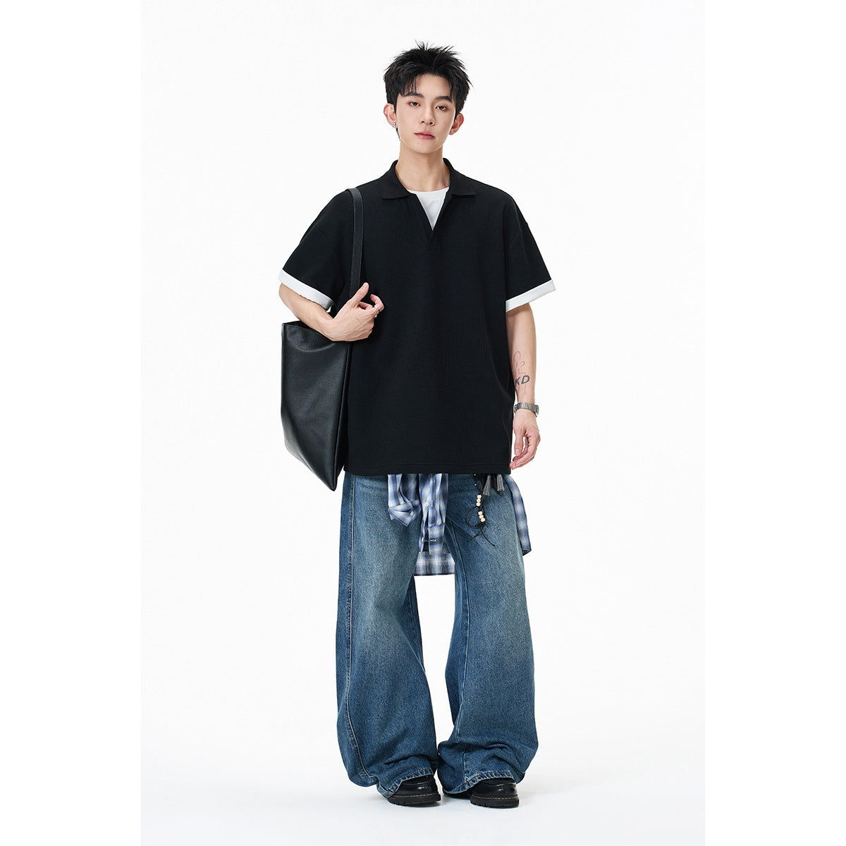 Model wearing a black short-sleeve polo with white sleeve cuffs, styled with wide-leg jeans.