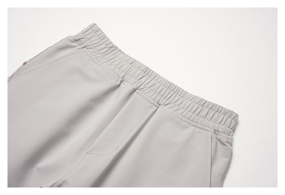Close-up of light gray trousers showing the gathered elastic waistband and angled front pocket openings.