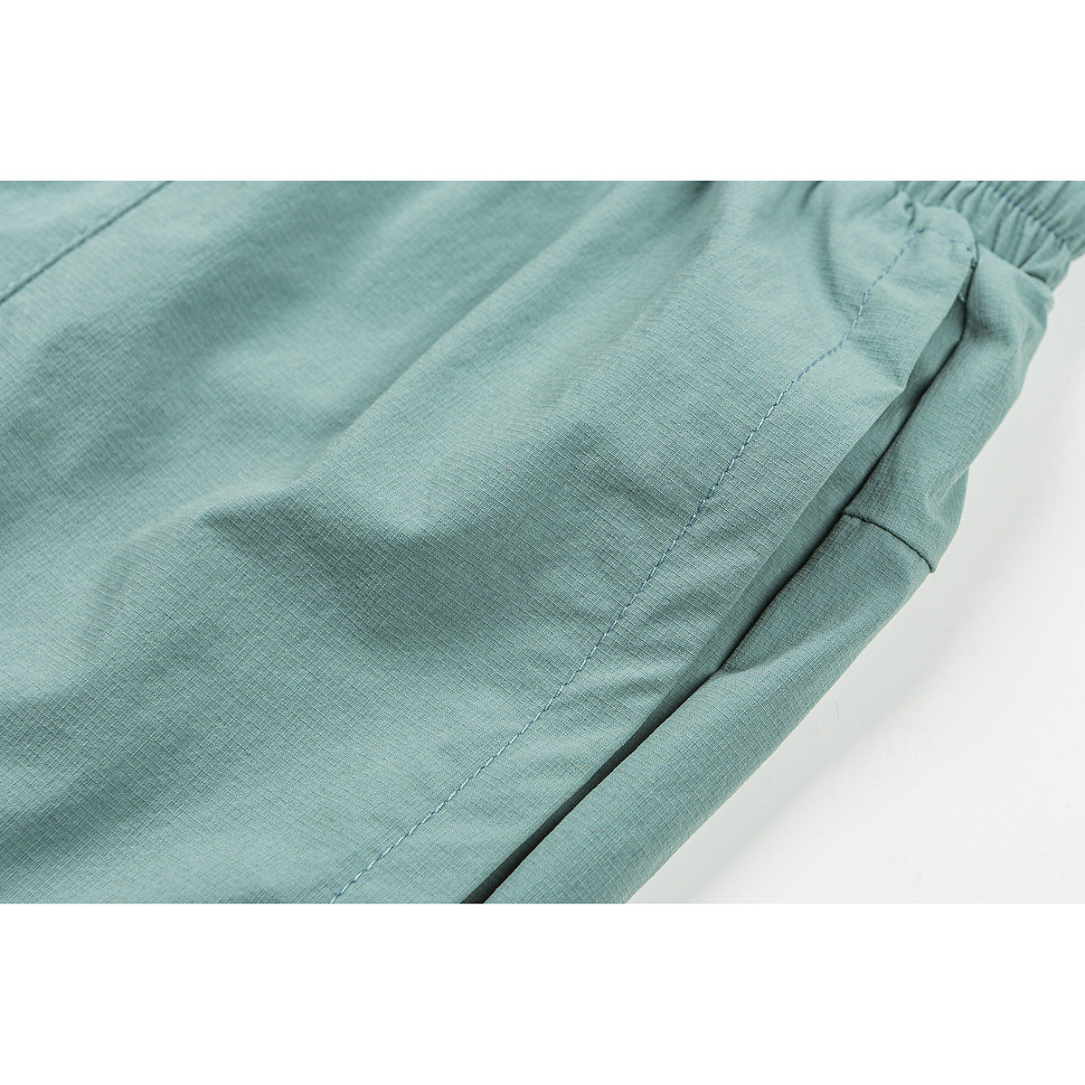 Close-up of aqua shorts showing the side seam, pocket edge, and fabric surface.
