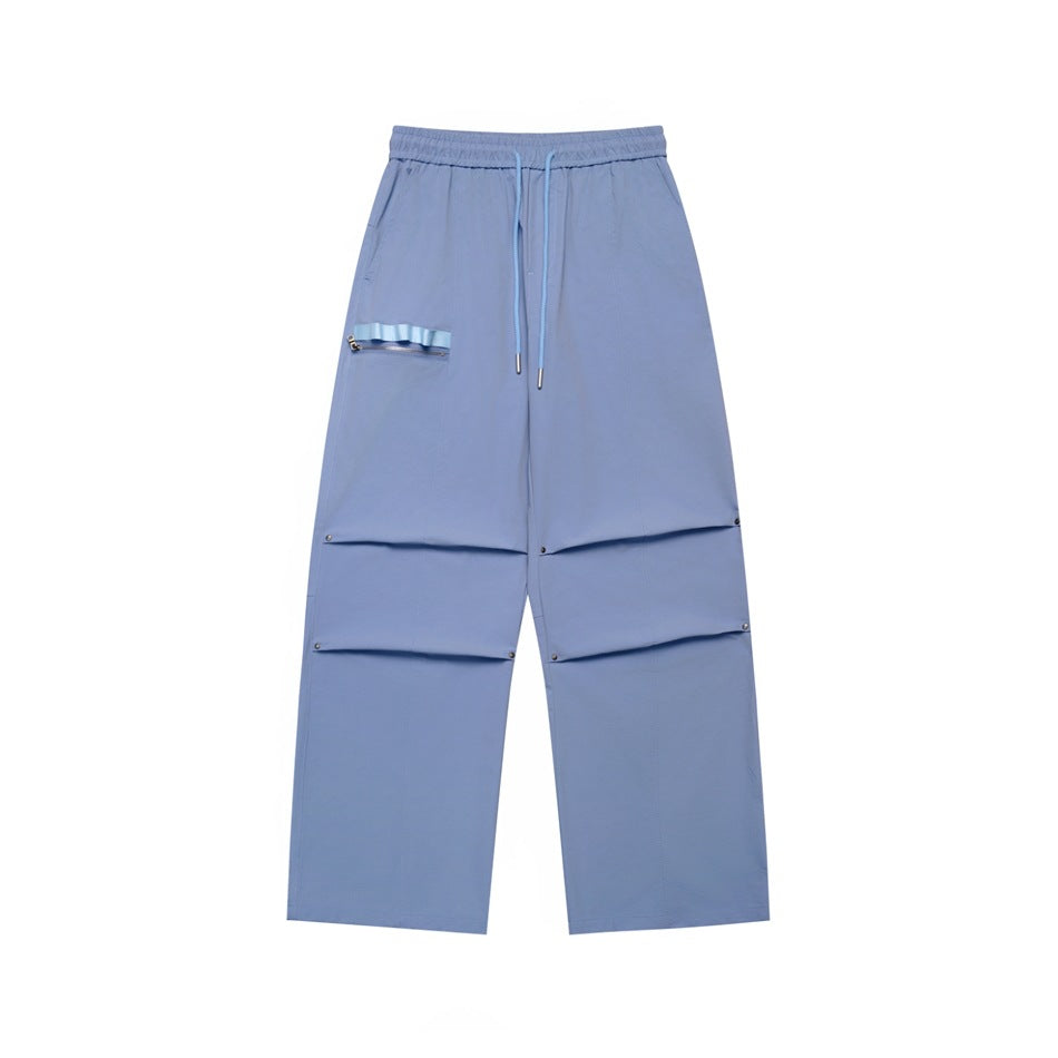 Blue wide-leg drawstring pants with knee pleats, rivets and a zippered ribbon pocket, flat lay front view