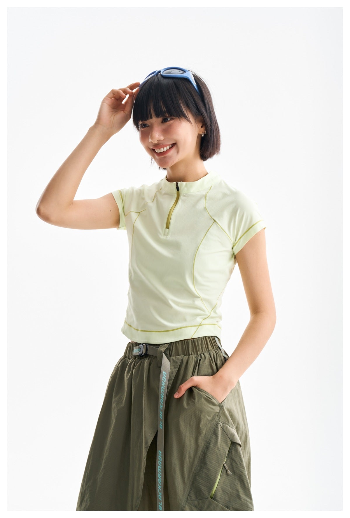 Model wearing a pale yellow short-sleeve zip top with contrast seams and an olive skirt.