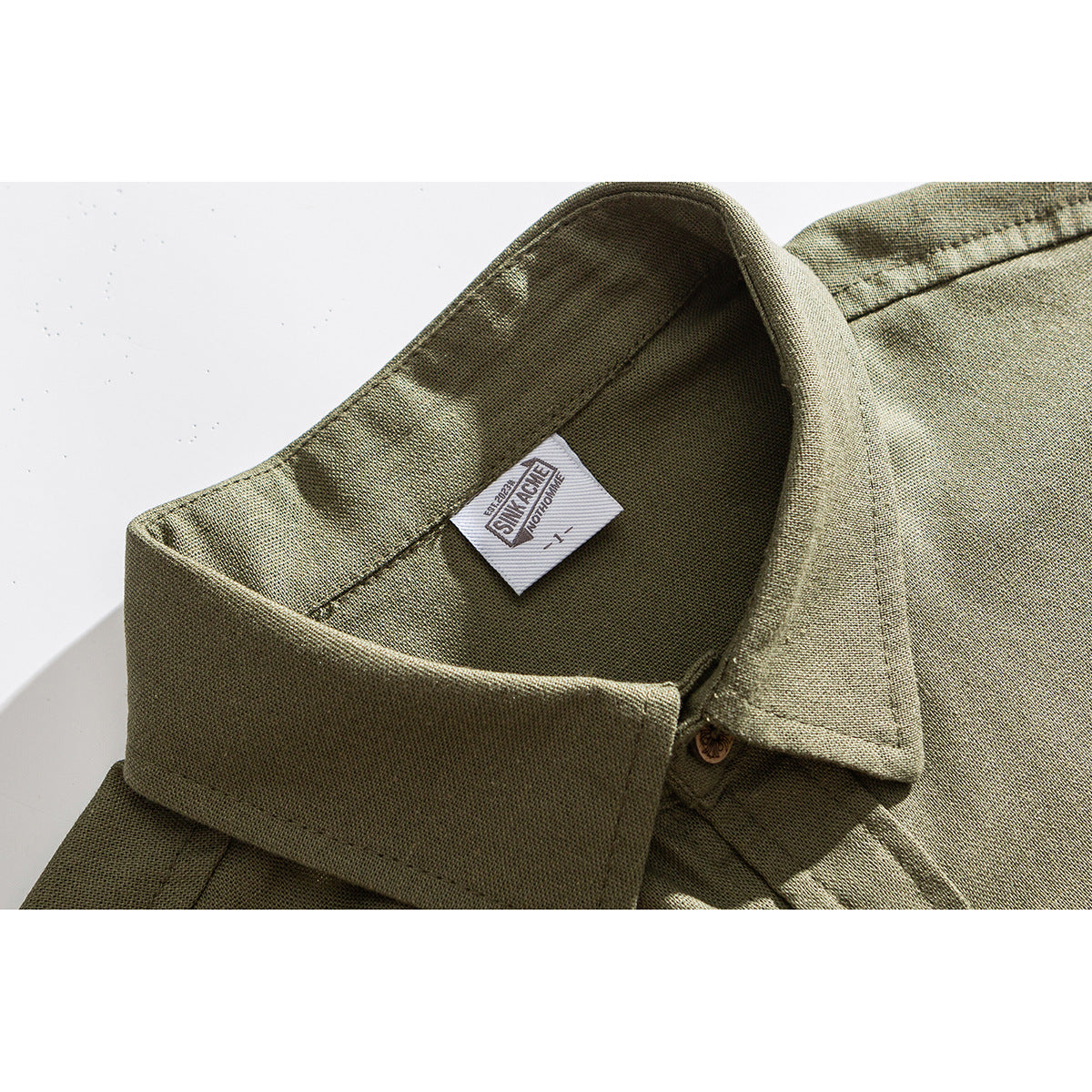 Close-up of the olive shirt's pointed collar, button, textured fabric, and sewn-in neck label.