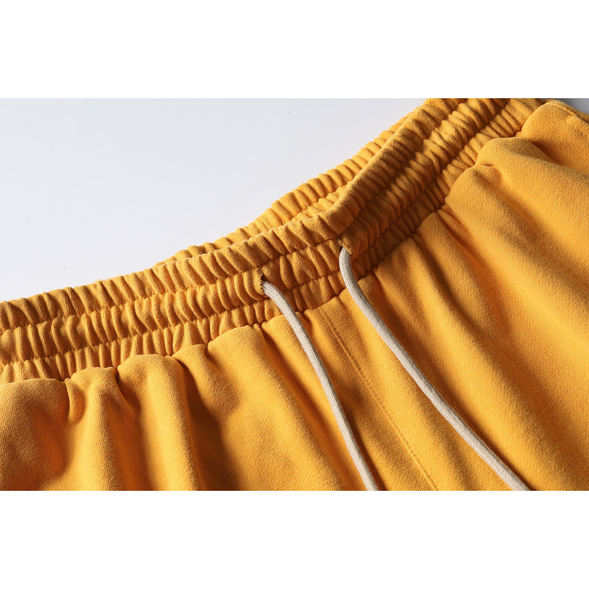 Close-up of mustard-yellow shorts showing a gathered elastic waistband and two white drawstrings.