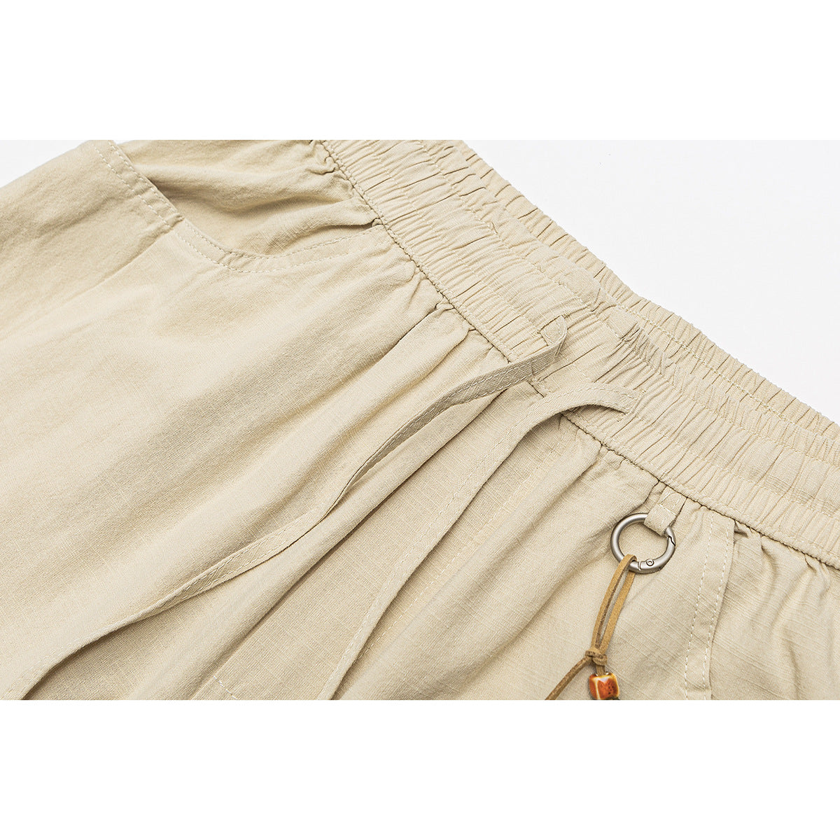 Close-up of beige pants showing the elastic waistband, pocket stitching, metal ring and beaded drawcord.