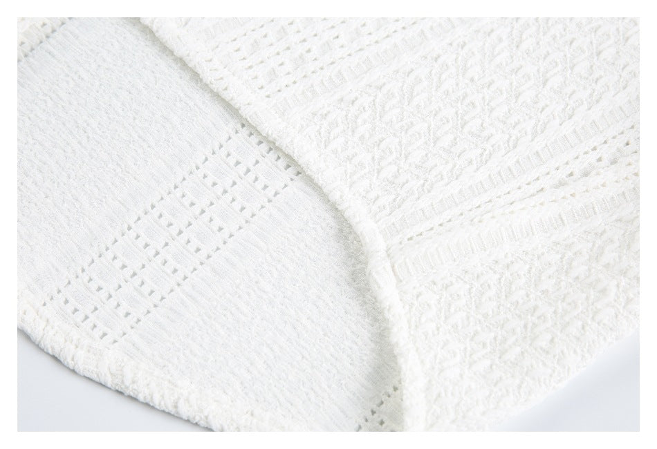 Close-up of white knit garment showing a seam and contrasting openwork bands beside a textured panel.