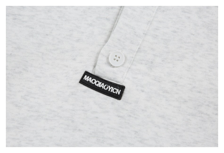 Close-up of a white button and black brand tab on the light gray heather shirt placket.