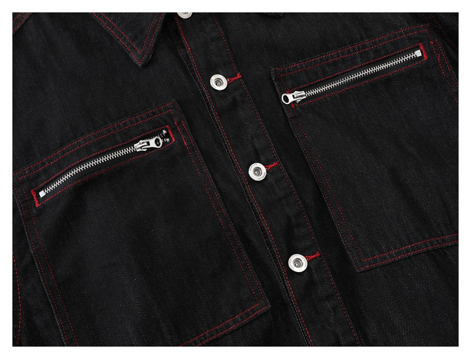 Close-up of a black denim jacket front with two zip pockets, silver snaps, and red stitching.