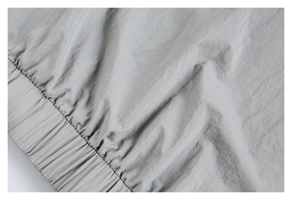 Close-up of gathered stitching where a light gray garment panel meets a wide elasticized edge.