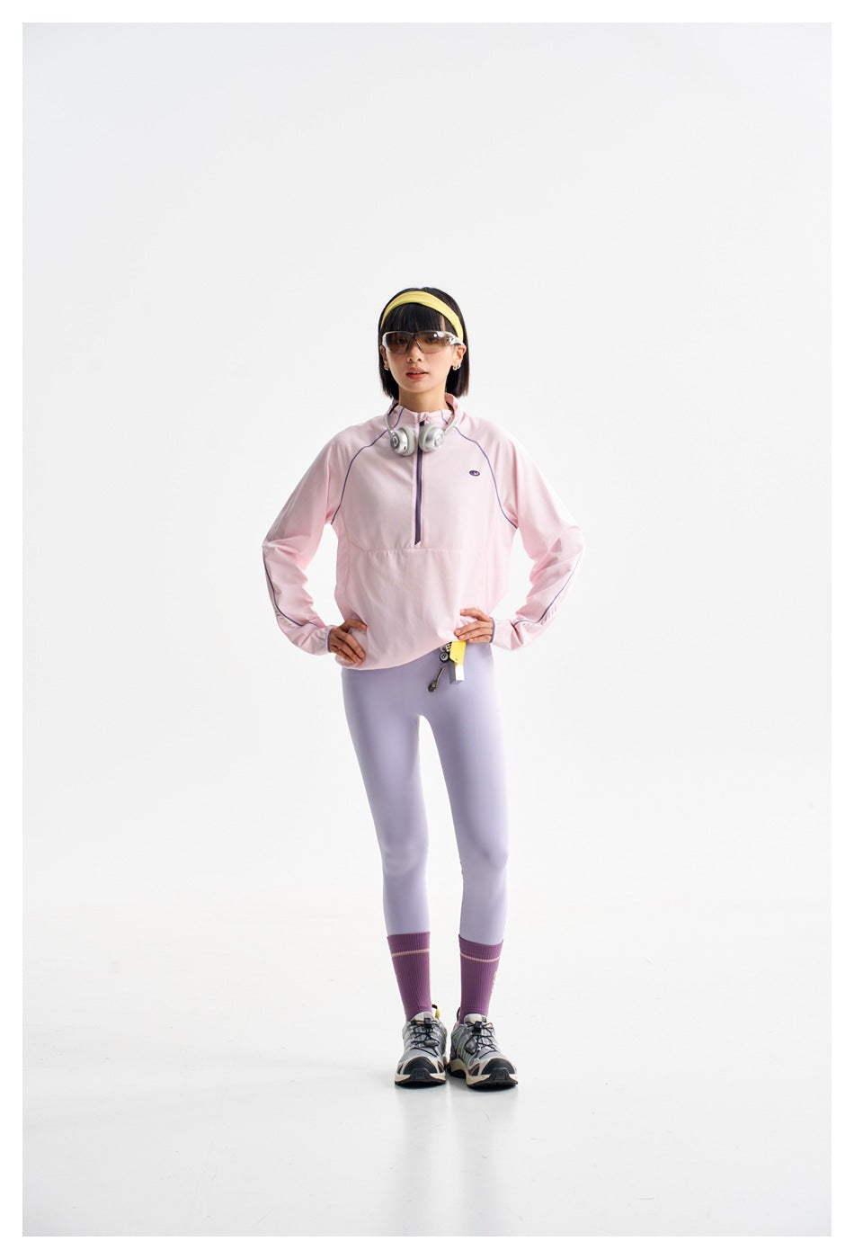 Full-length model in a pale pink half-zip top and light lavender leggings, standing with hands on hips.
